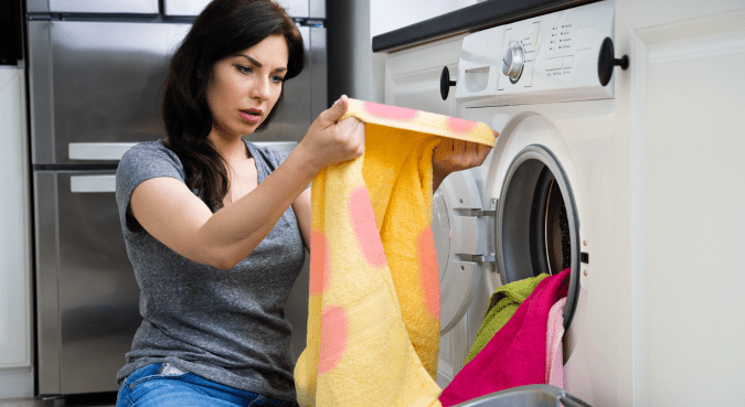 A woman looks at a towel she just pulled from the washing machine.