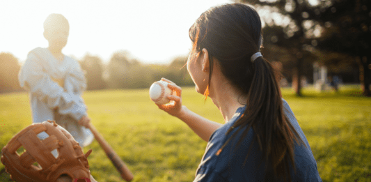 A mom throws a baseball to her son at bat.