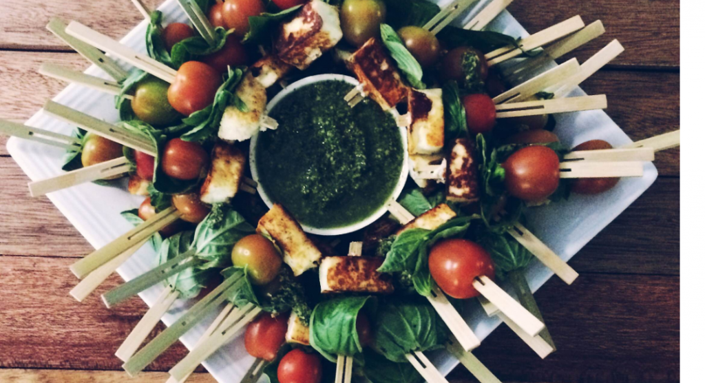 plate with holiday appetizers caprese skewers and pesto dipping sauce