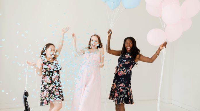 Three women cheering and holding balloons while throwing pink and blue confetti