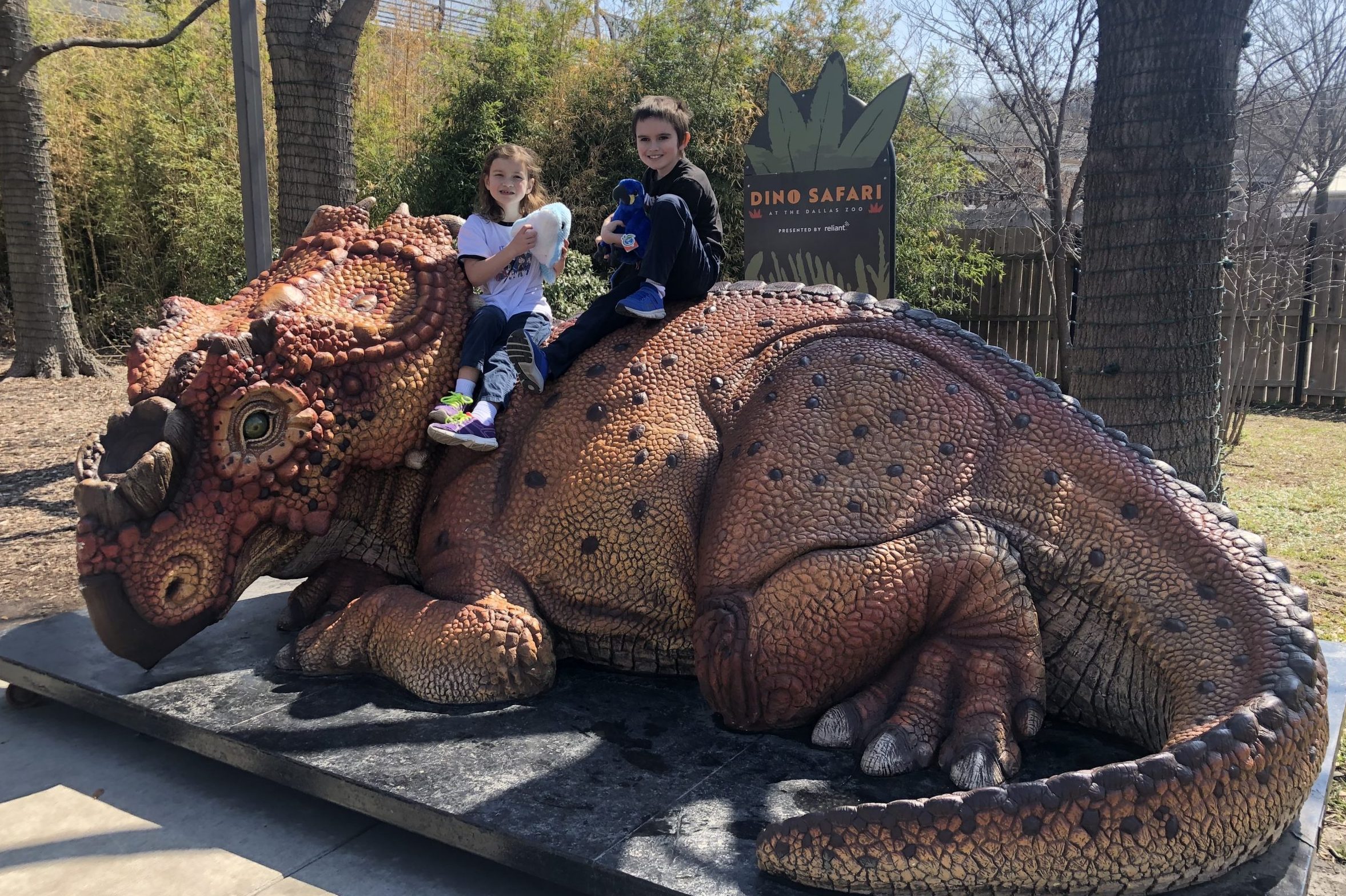 Children sitting on a dinosaur statue at the Dallas Zoo, Dallas Zoo Dino Safari review.