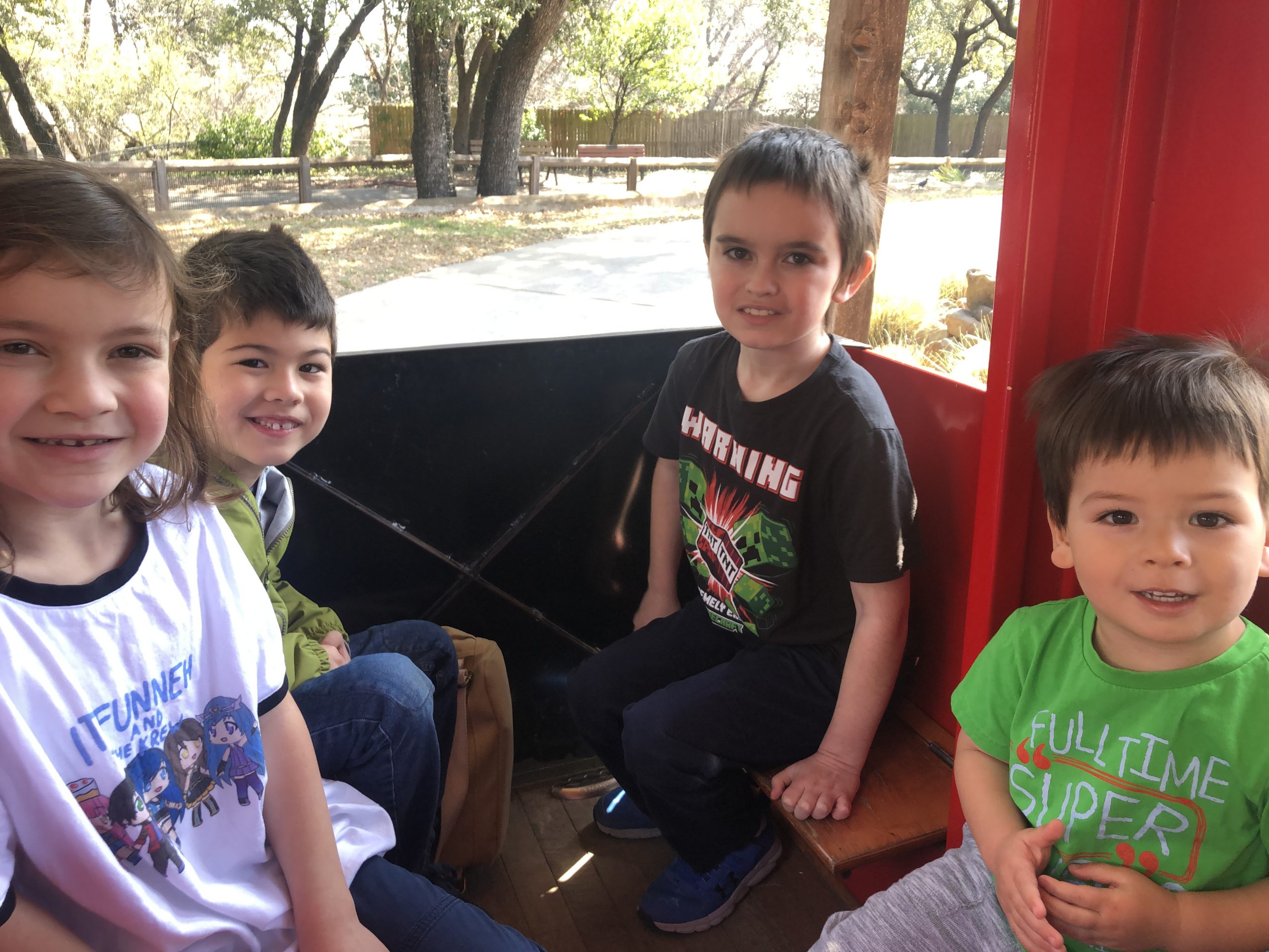 Four children smile at the camera while sitting on a train ride at the Dallas Zoo