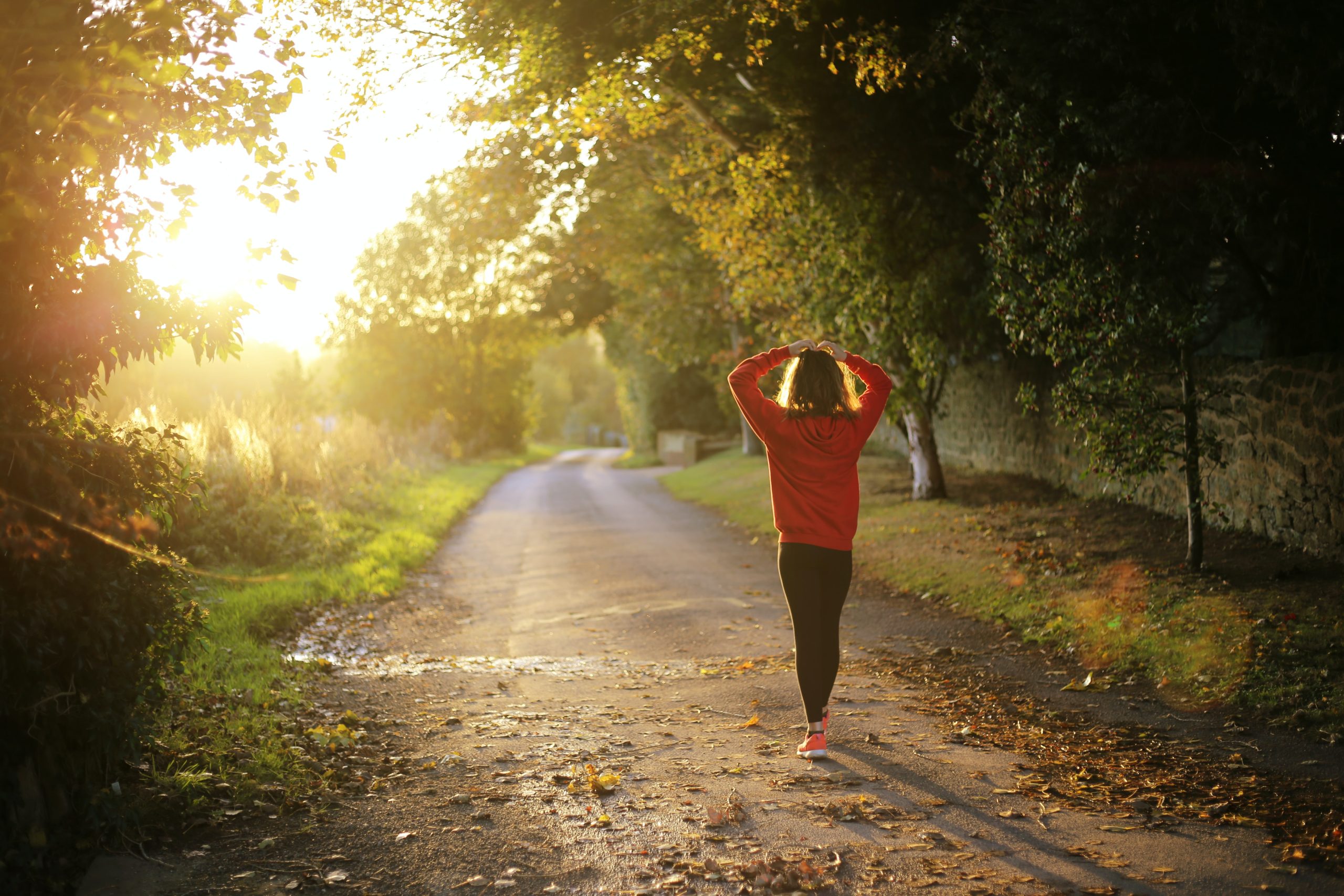 A woman walks down a running path with her hands on her head.