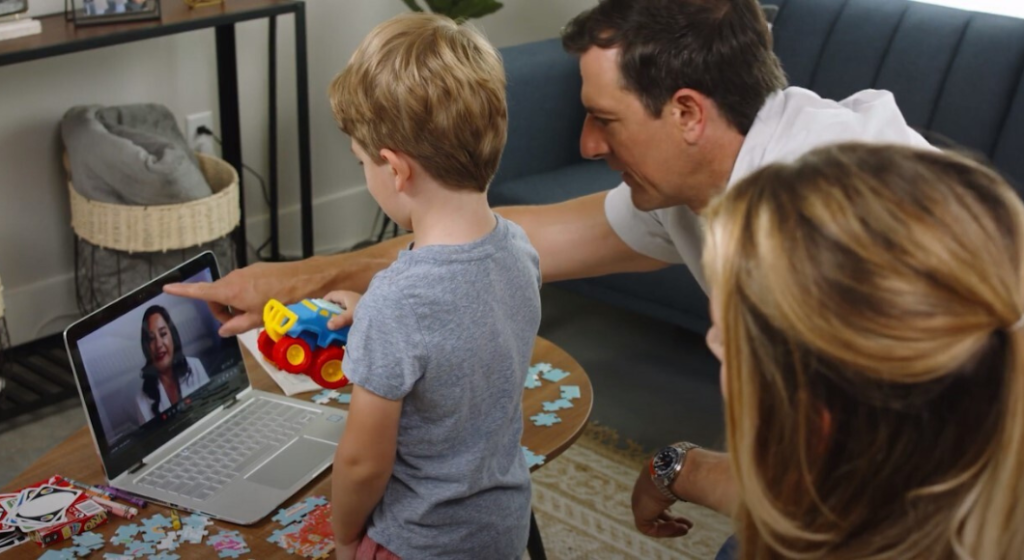 A child and his parents look at a computer screen with a telehealth professional.