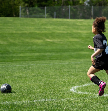 Young girl running toward a soccer ball on an open soccer field