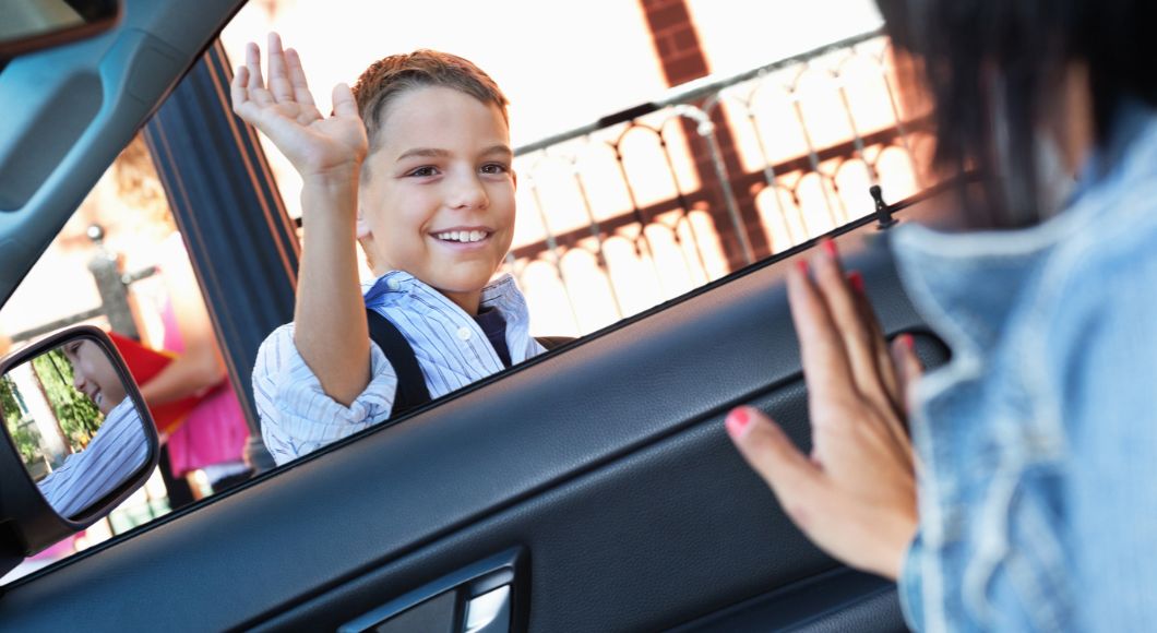 Boy happily waves bye at mom who is sitting in her car.