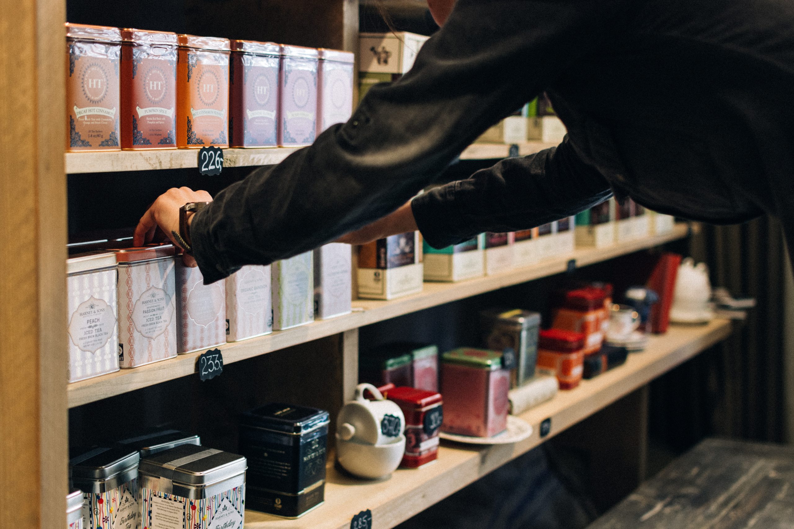 A shopper reaches for a box of tea on a shelf stacked with an assortment of different teas.