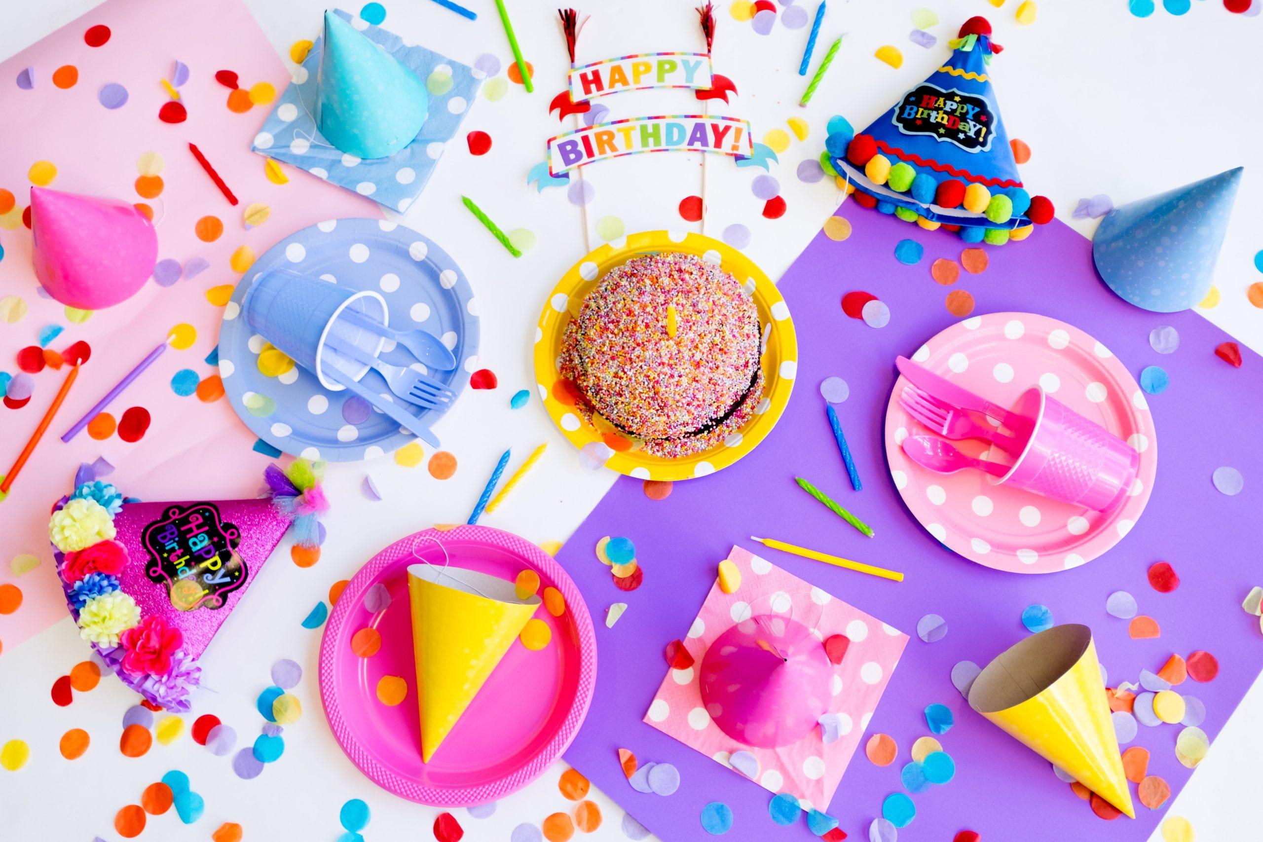 A table with plates, birthday hats, confetti, and cake.