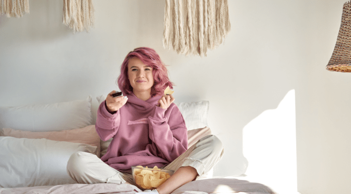 A woman lays in bed with chips while watching tv.