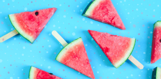 frozen slices of watermelon with Popsicle sticks in them, laying on a bright blue background with splotches of color throughout