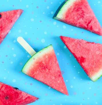 frozen slices of watermelon with Popsicle sticks in them, laying on a bright blue background with splotches of color throughout
