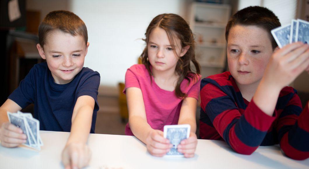 Three young children sit by each other as they play a game of Uno.