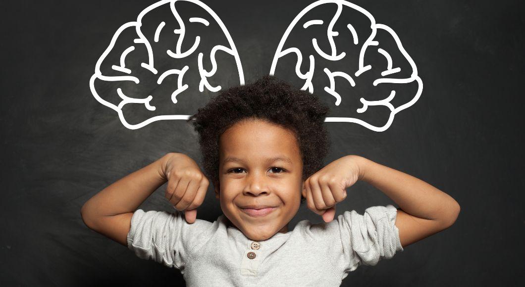 Young boy smiles as he flexes his muscles in front of a drawing of a brain.