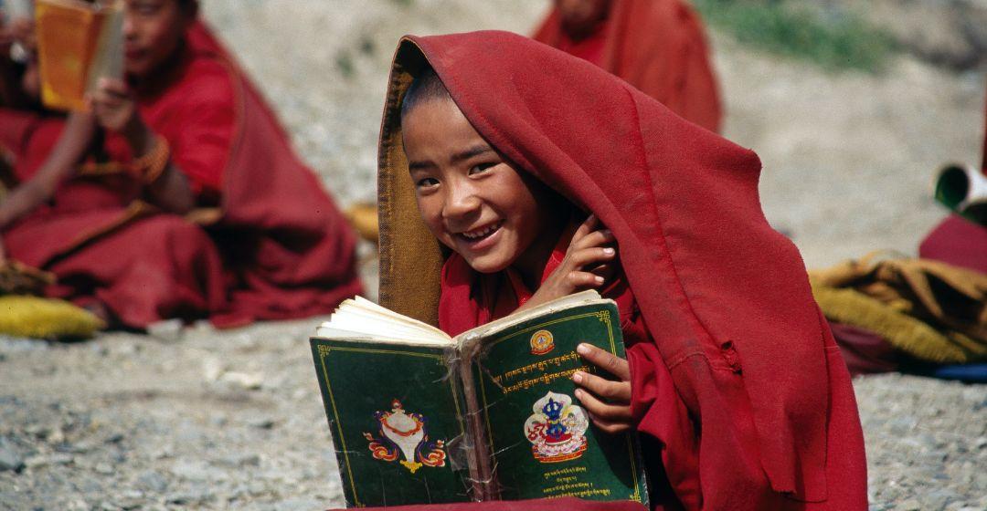 A child reads a book with a blanket over his head.