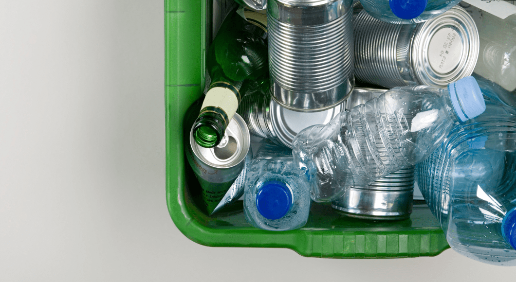 A green recycling bin with plastic bottles and tin cans.