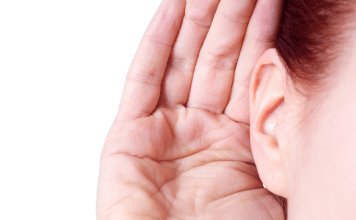 A woman holds her hand up to her ear to listen to noises.