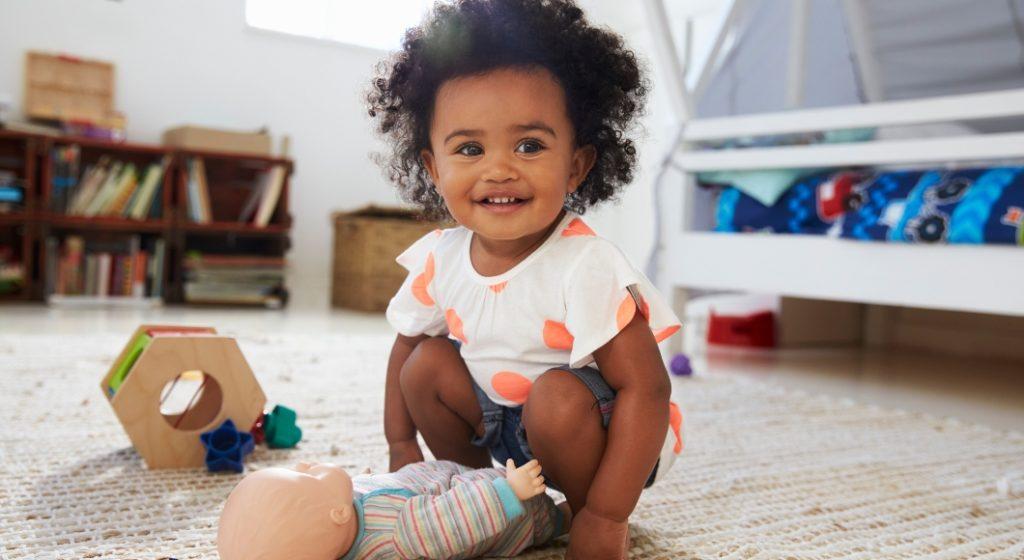 toddler girl smiling and playing with a baby doll