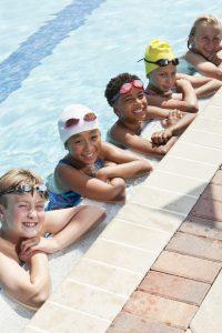 Several kids rest on the ledge of a pool.