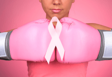 A woman wears two pink boxing gloves with a breast cancer ribbon on top.