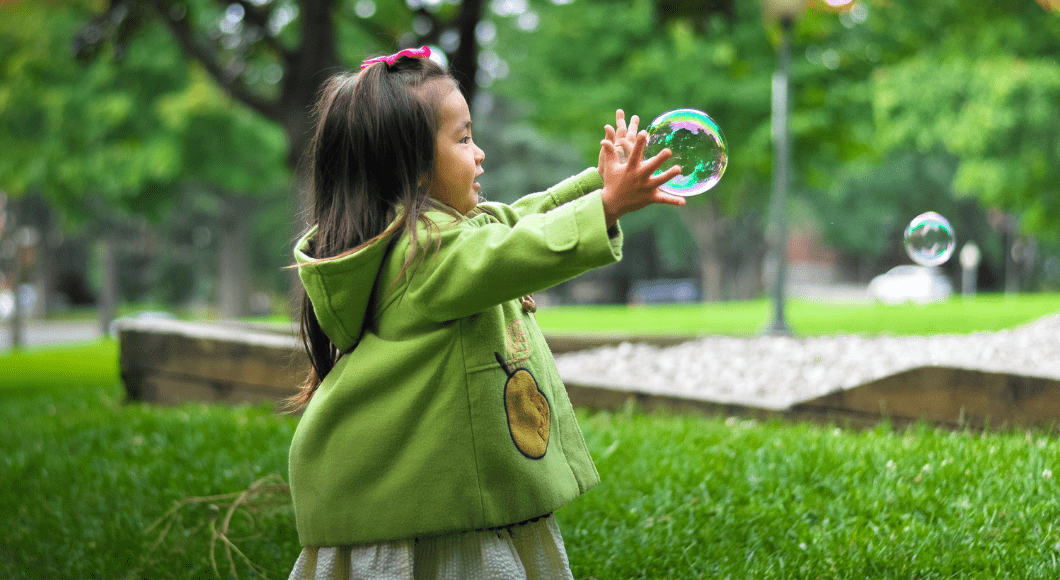 A toddler girl catches bubbles outside.