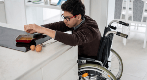A teenage boy in a wheelchair cooks.