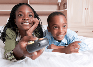 Two kids watch tv while the girl holds a remote.
