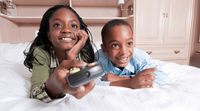 Two kids watch tv while the girl holds a remote.