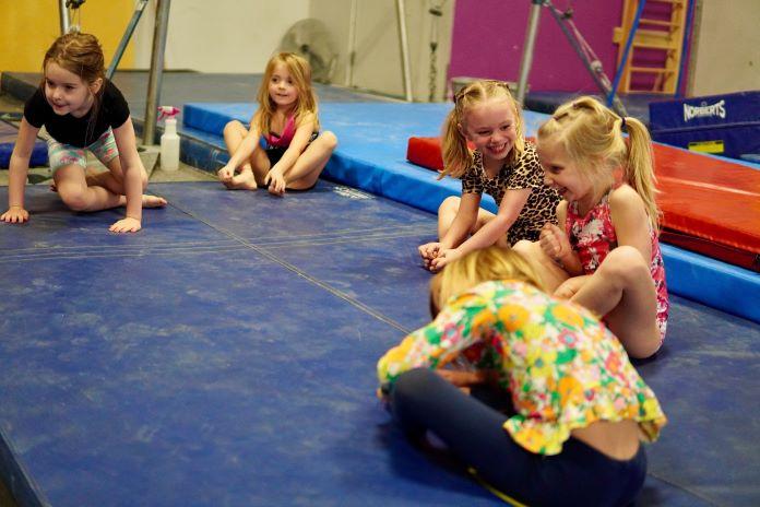 A group of preschool aged girls stretch in a circle during a gymnastics class.
