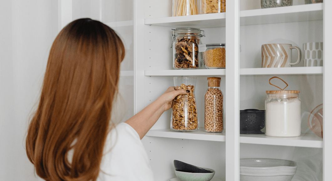 A woman reaching for a jar in a tidy pantry.