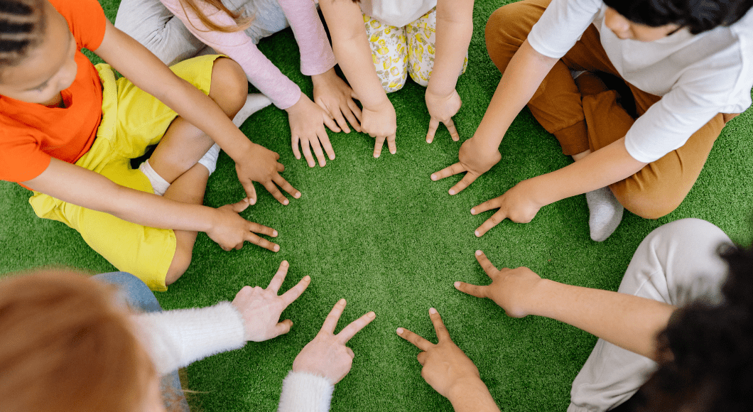 Circle of diverse children and adults sitting on turf showing their hands
