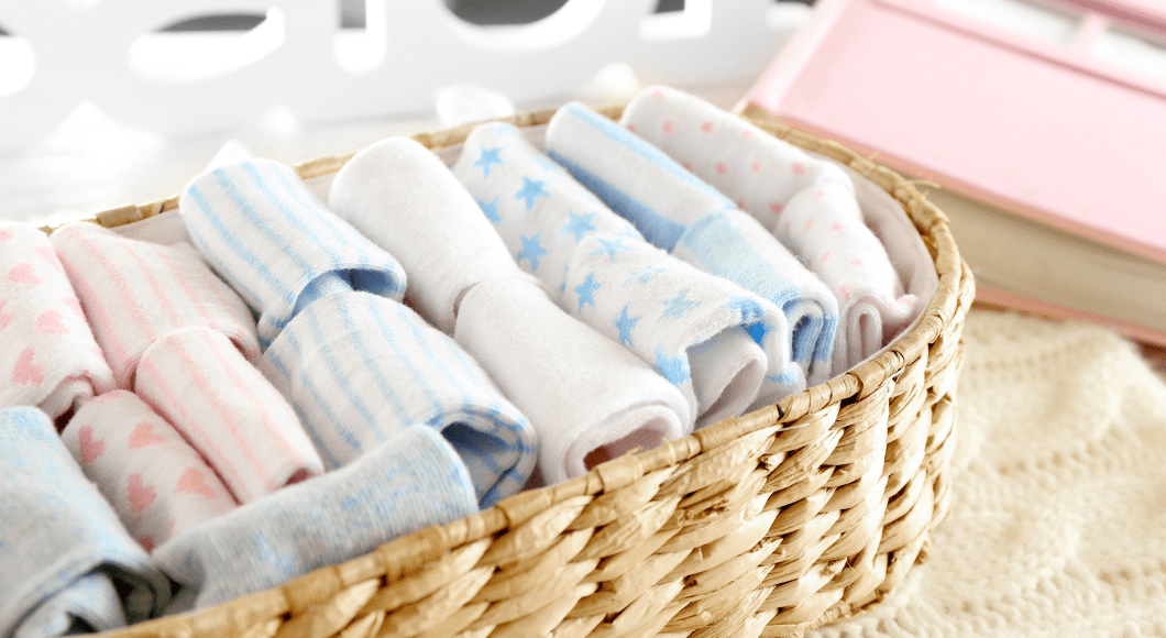 A basket of baby clothes and washcloths file folded for organization.