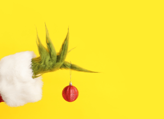 The Grinch's hand holding a red ornament with a yellow background