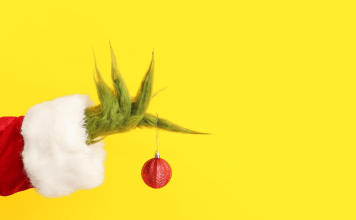 The Grinch's hand holding a red ornament with a yellow background