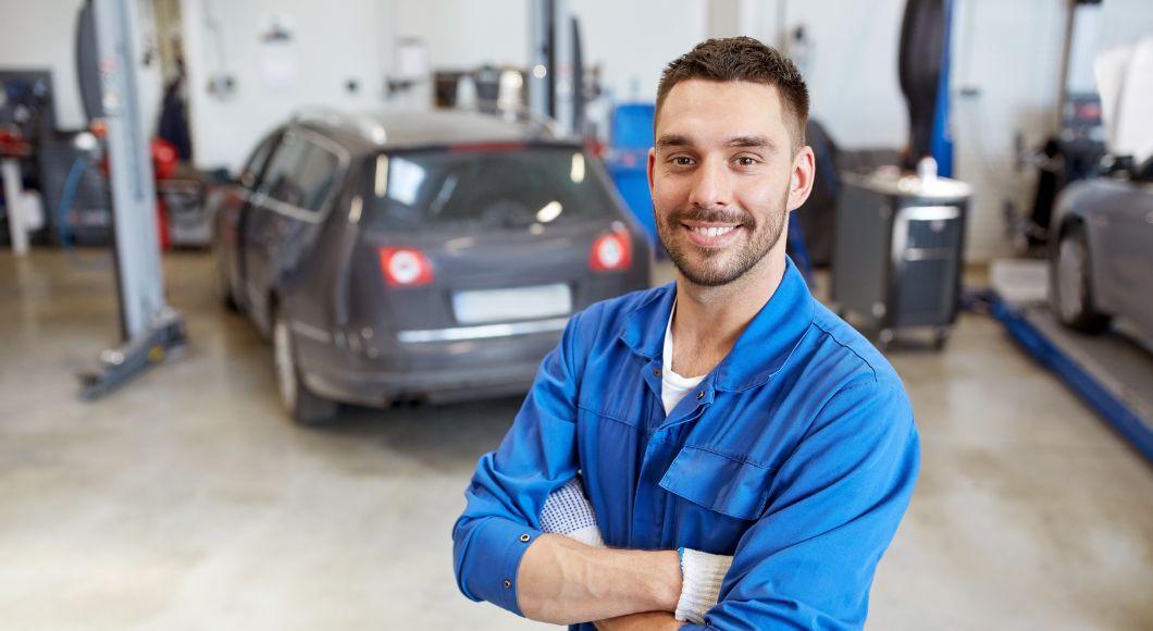 Young male auto technician poses in front of car in an auto repair bay.