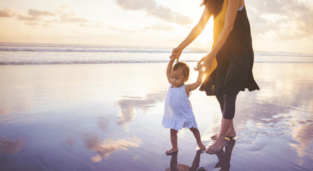 Mother and child walk in the sand together at dusk