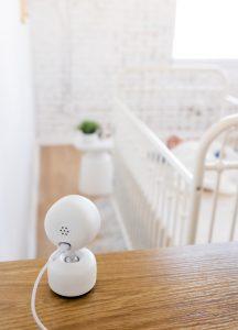 A baby monitor camera sits on the dresser facing baby napping in his crib.
