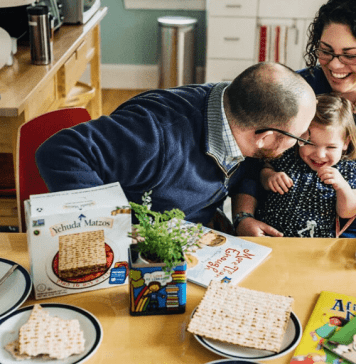 A mom, dad, and young daughter celebreate passover with books and matzah on a table