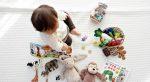 Infant with dark hair plays on a white rug surrounded by colorful toys.