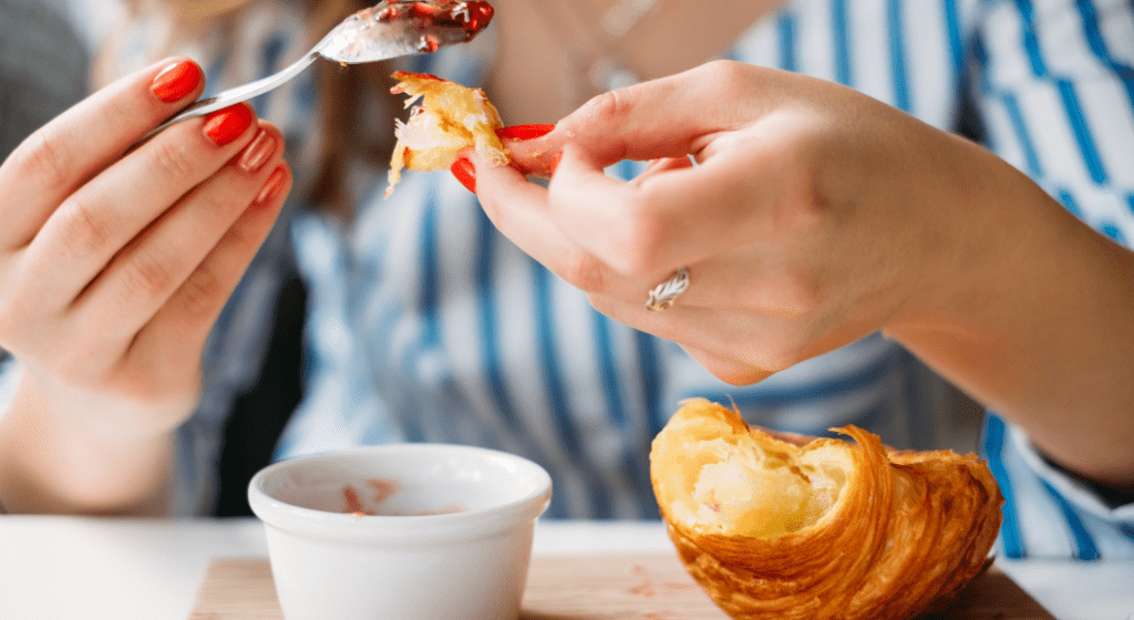 Woman spoons jam onto a flaky croissant for brunch.