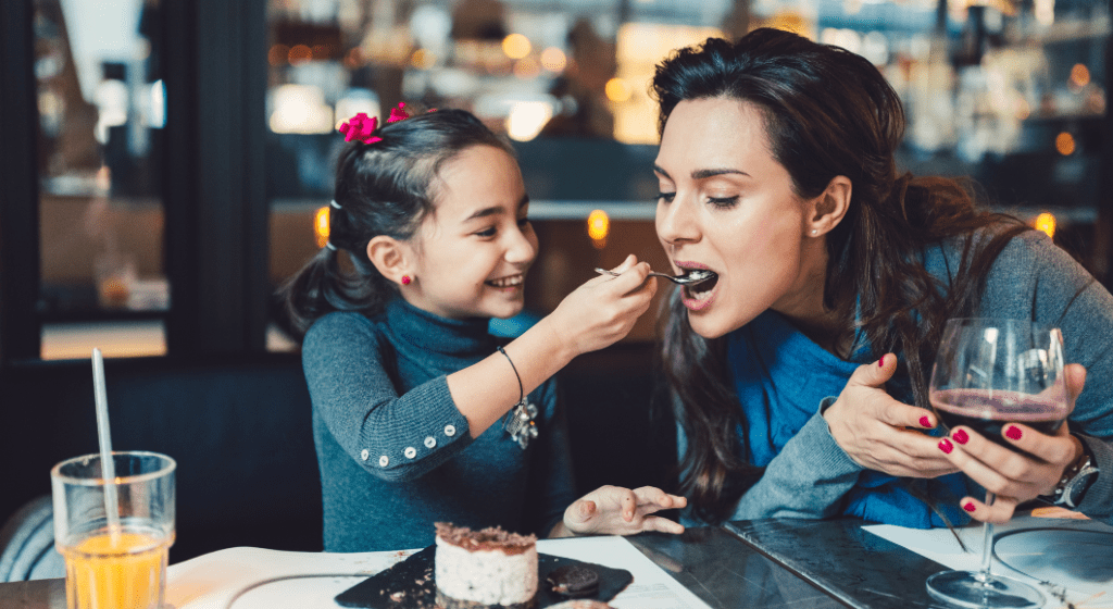 Little girl spoon feeds her mom dessert at a restaurant for Mother's Day brunch.